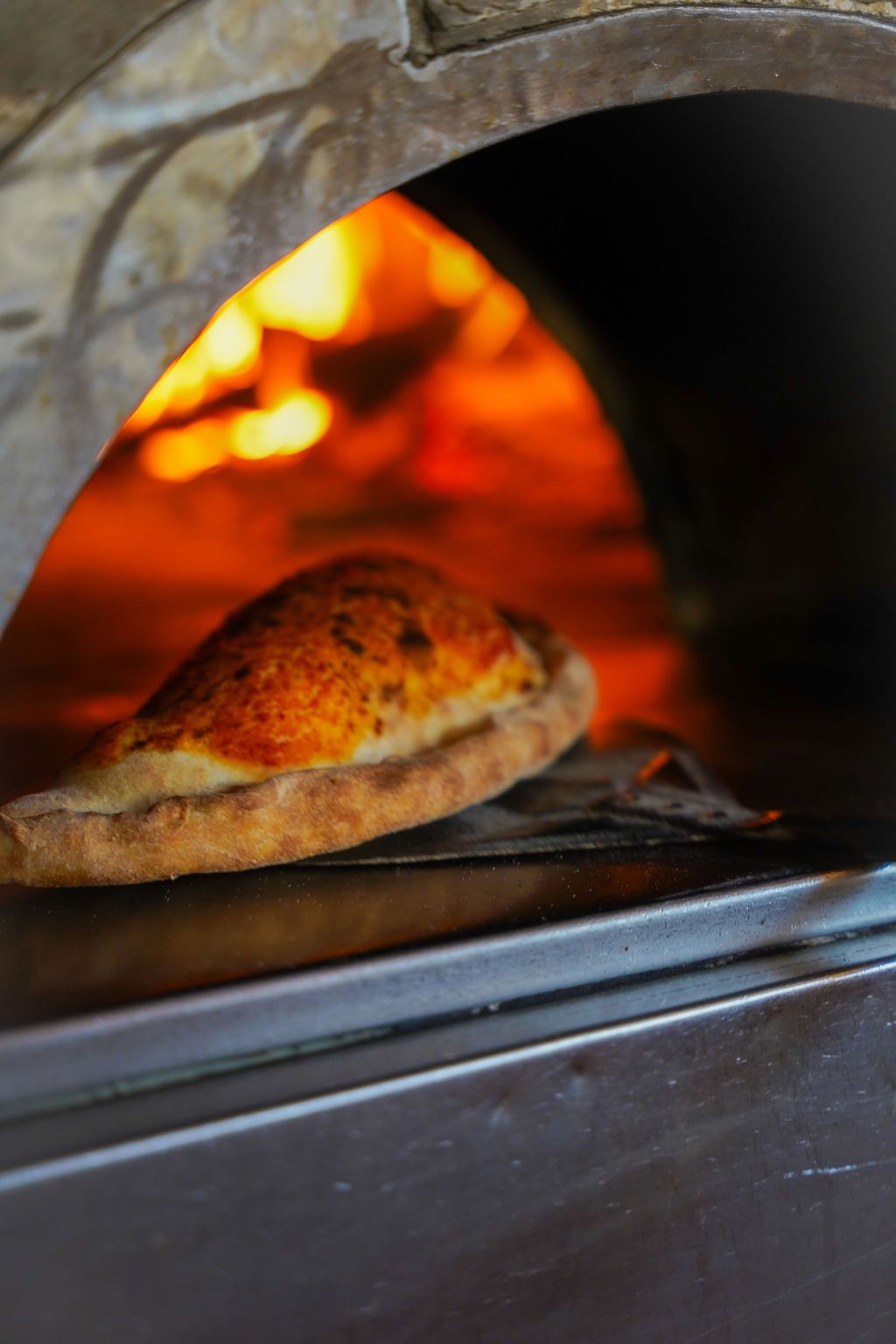 Una pagnotta di pane che cuoce in un forno a legna con fiamme ardenti.
