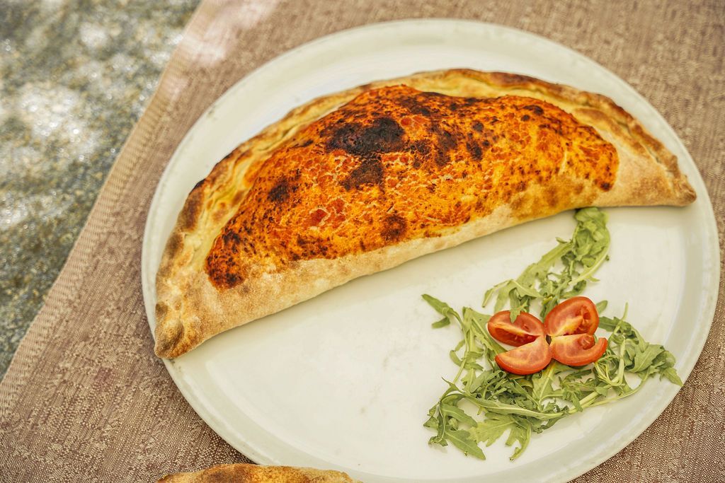 Focaccia ripiena e cotta al forno, servita su un piatto bianco con guarnizione di pomodoro e verdure.