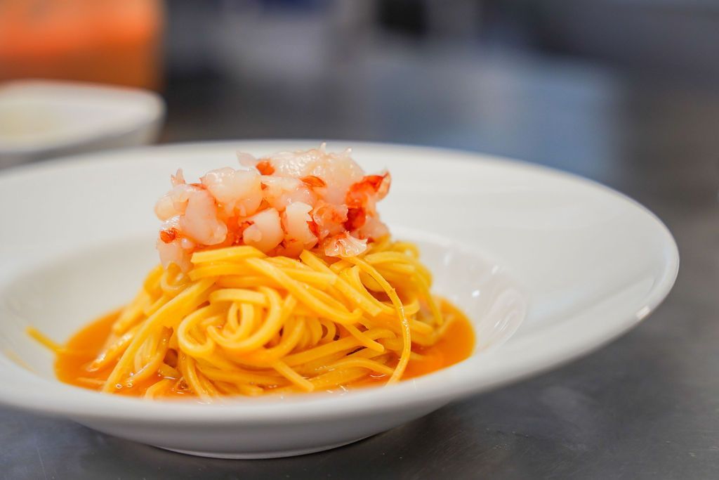 Piatto bianco con spaghetti al sugo d'arancia e gamberetti tritati.