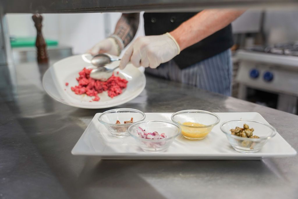 Lo chef impiatta la frutta rossa a cubetti su un vassoio con piccole ciotole di ingredienti in una cucina