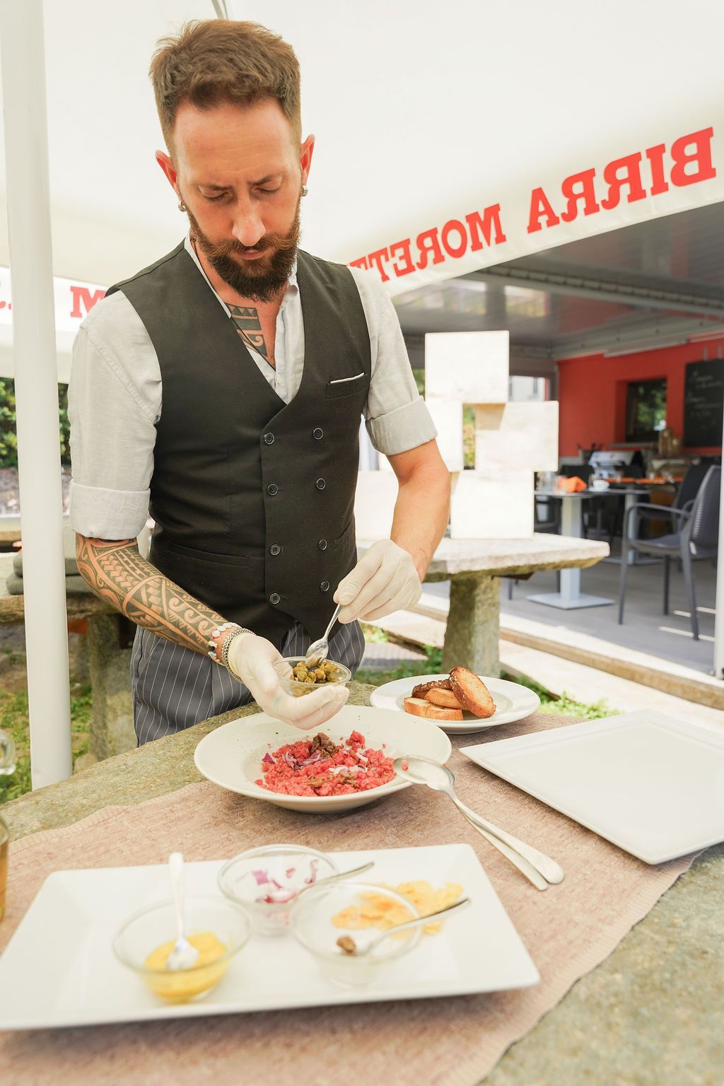 Lo chef impiatta una pietanza gourmet su un vassoio al bancone di un ristorante all'aperto.