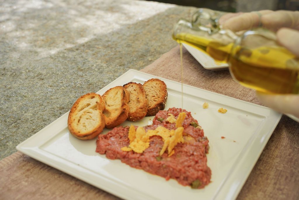 Piatto con fette di pane tostato, crema rosa ricoperta di formaggio giallo e olio d'oliva versato a lato.