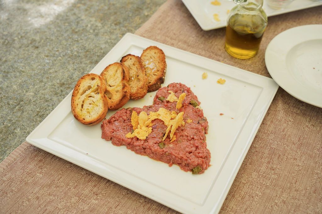 Su un tavolo sono disposti toast e fette sottili di carne, con accanto una piccola bottiglia di vetro.
