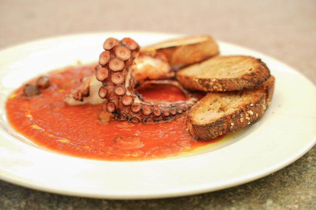 Piatto di frutti di mare con salsa di pomodoro, guarnizione di tentacoli e fette di pane grigliato.