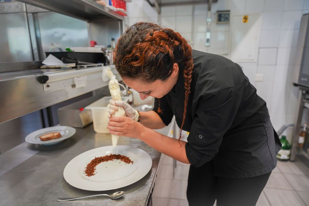 Uno chef che decora un piatto bianco con la salsa in una cucina professionale.