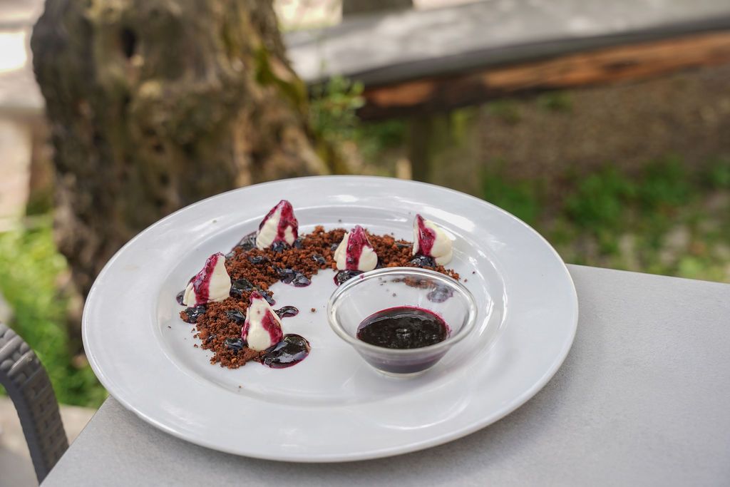 Piatto da dessert bianco con composizione artistica di frutti di bosco e salsa, su un tavolo all'aperto.
