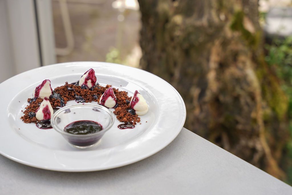 Piatto da dessert bianco con pezzi di pasta frolla guarniti con frutta e una ciotolina di salsa su un tavolo all'aperto.