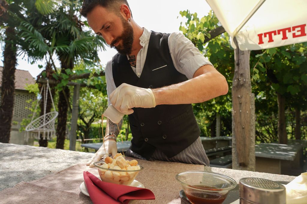 Lo chef impiatta il dessert all'aperto su un tavolo rustico, spolverando con zucchero a velo una ciotola di pasticcini.