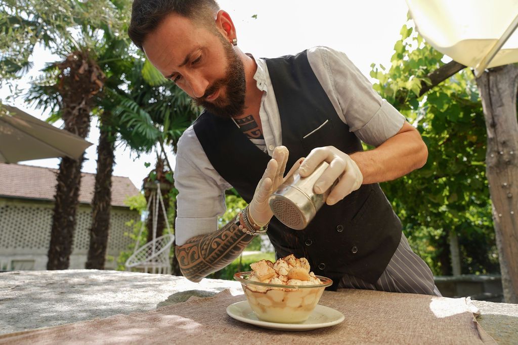Una persona con i guanti spreme della salsa su un dessert impiattato all'aperto.
