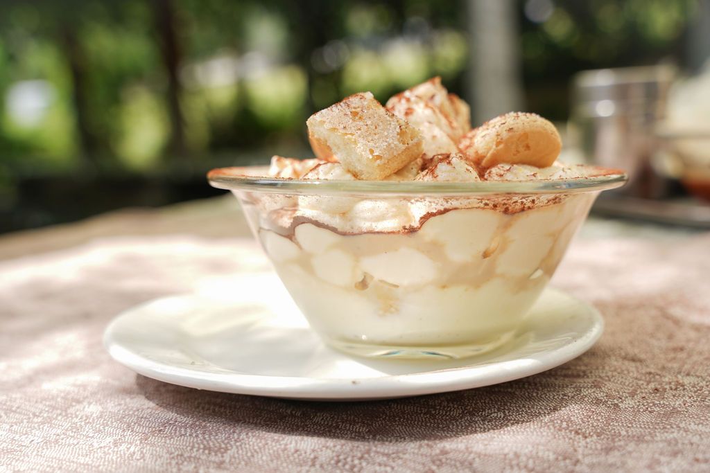 Ciotola di vetro con cremoso dessert guarnito con pezzetti di zucchero e cannella su un piattino bianco all'aperto