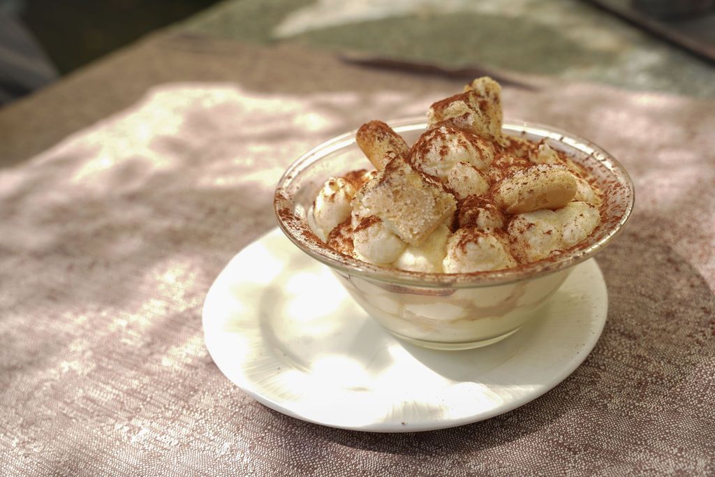 Ciotola di vetro per dessert cosparsa di cannella su un piattino bianco, all'aperto su una tovaglia.