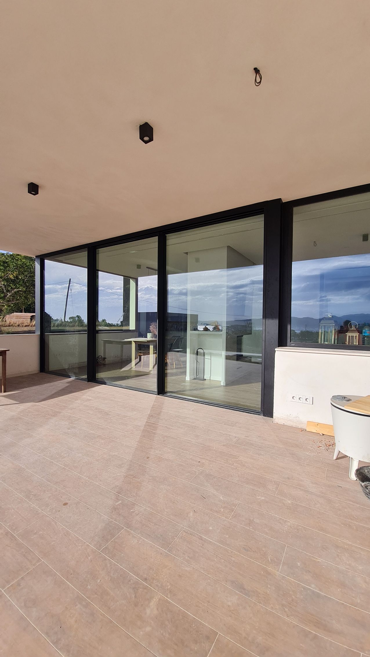 Entrada moderna al edificio con puertas de cristal, un patio cubierto y una terraza embaldosada con vistas al paisaje.