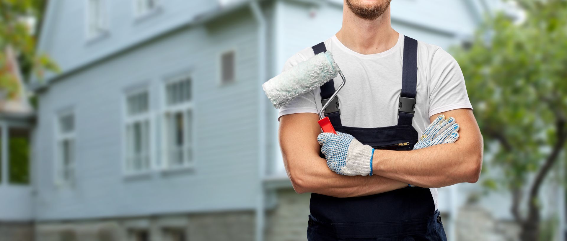 Un artisan avec un rouleau de peinture devant une maison