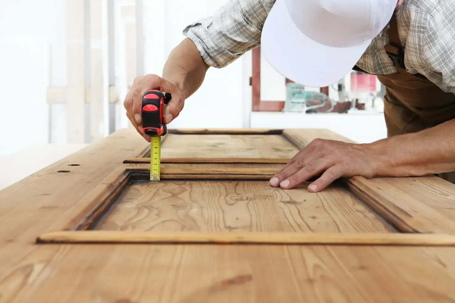 La persona mide el marco de una puerta de madera con una cinta métrica.