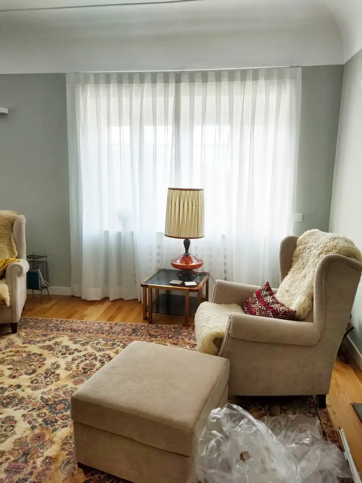 Una sala de estar con dos sillas, una otomana y una lámpara.