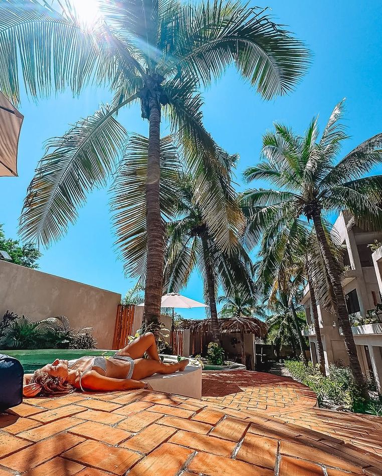 A woman is laying on a lounge chair under a palm tree.