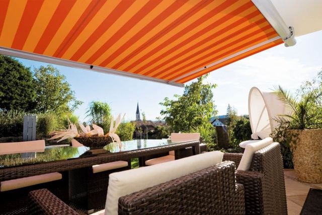 Brenig Instandsetzungs GmbH – orangerote Markise über Gartenmöbeln