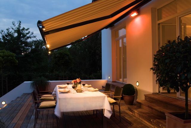 Brenig Instandsetzungs GmbH – weißer Tisch romantisch beleuchtet auf Terrasse, Markise darüber