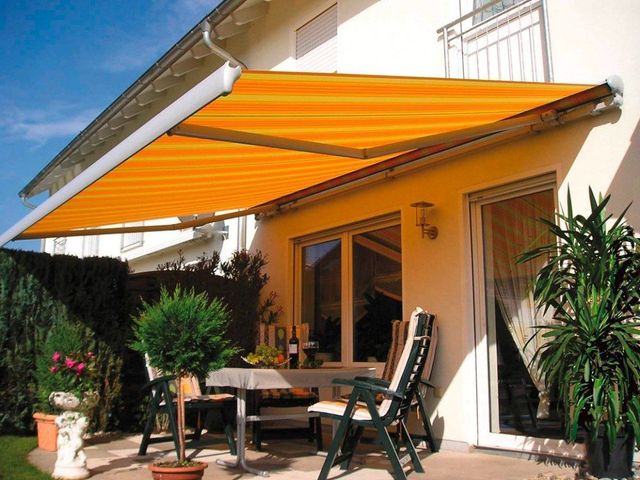 Brenig Instandsetzungs GmbH – eine gemütliche Terrasse in einem Garten mit einer gelbweißen Markise als Überdachung