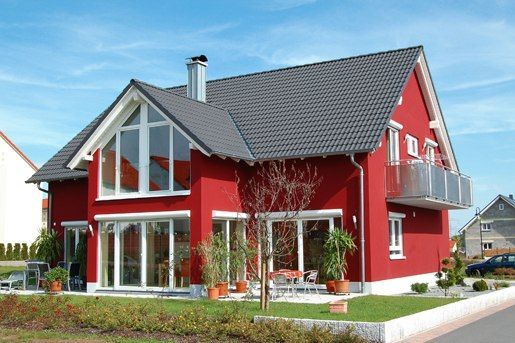 Brenig Instandsetzungs GmbH – ein rotes Haus mit großzügigen Glasfenstern und grüner Wiese vor blauem Himmel