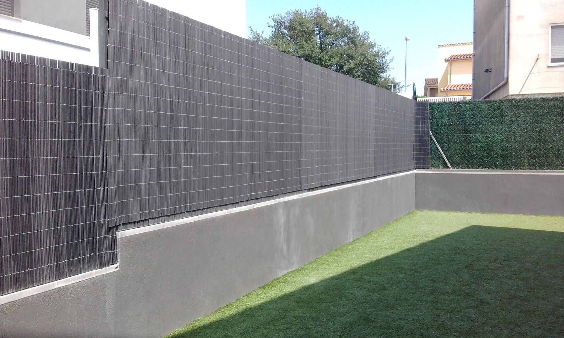 Una valla rodea una zona de césped con un edificio al fondo.