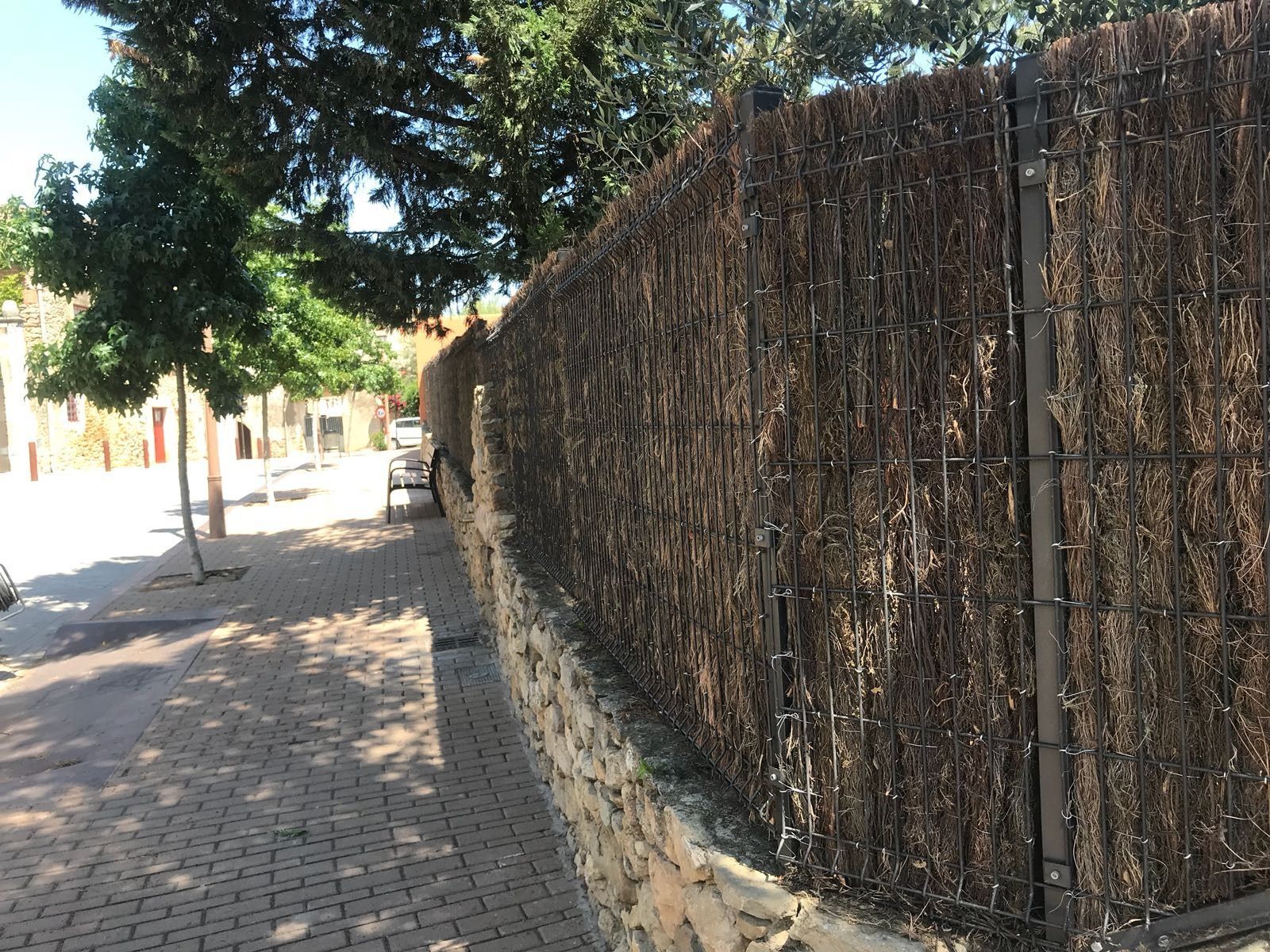 Una valla hecha de ramas está a lo largo del costado de una acera de ladrillos.