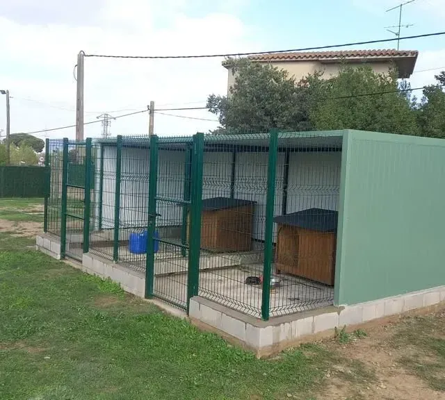 Una hilera de perreras con una valla verde alrededor de ellas.