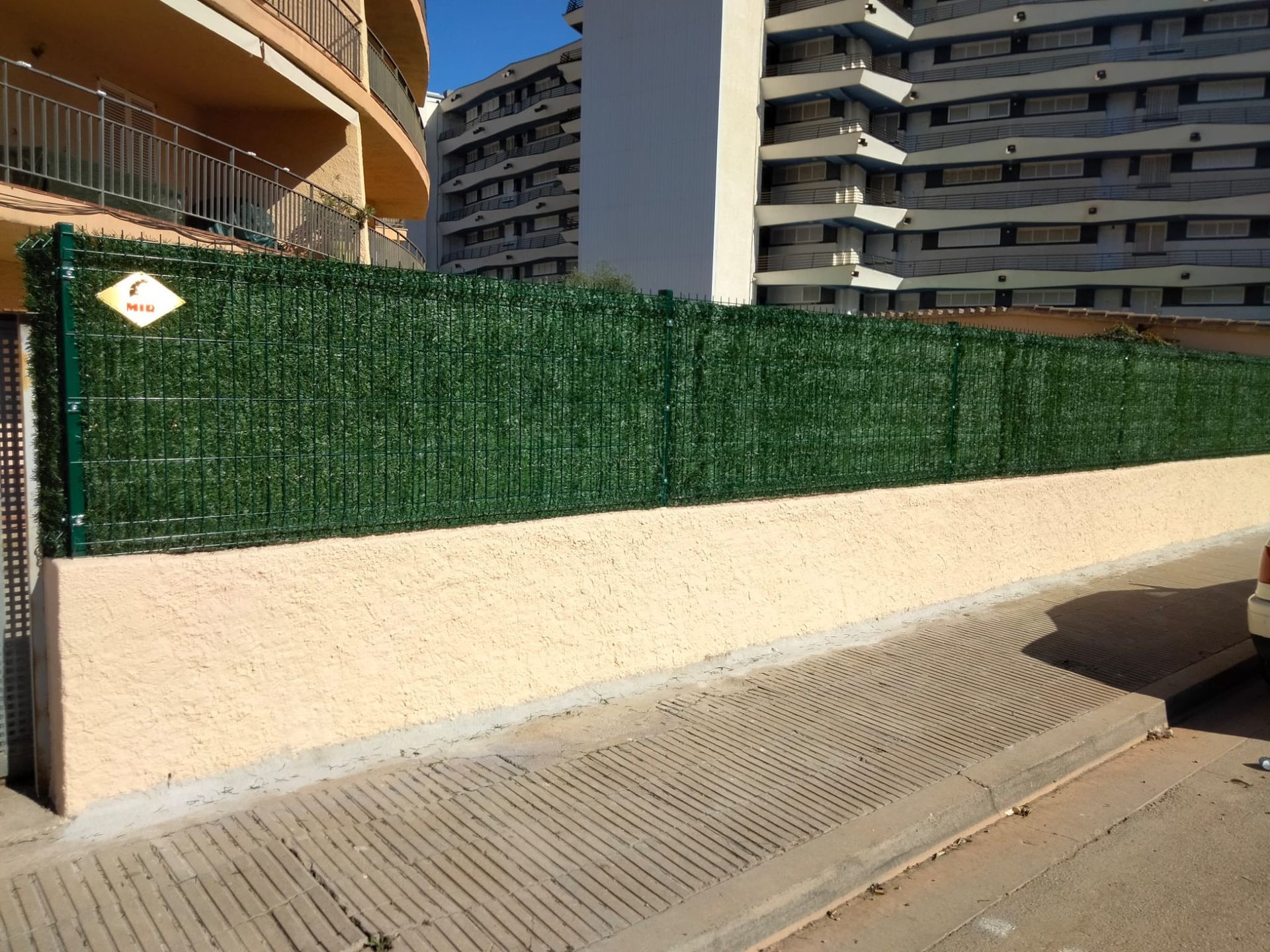 Un coche está aparcado delante de una valla con un edificio al fondo.