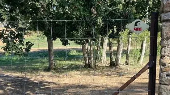 Una valla con árboles al fondo y un cartel en ella.