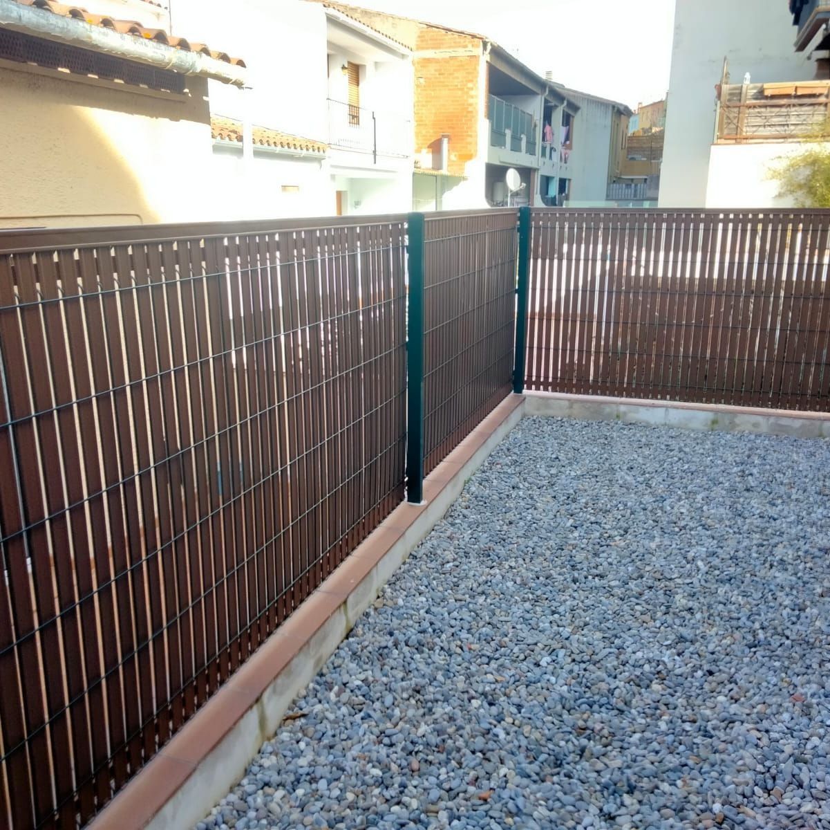 Una valla de madera rodea una zona de grava frente a un edificio.