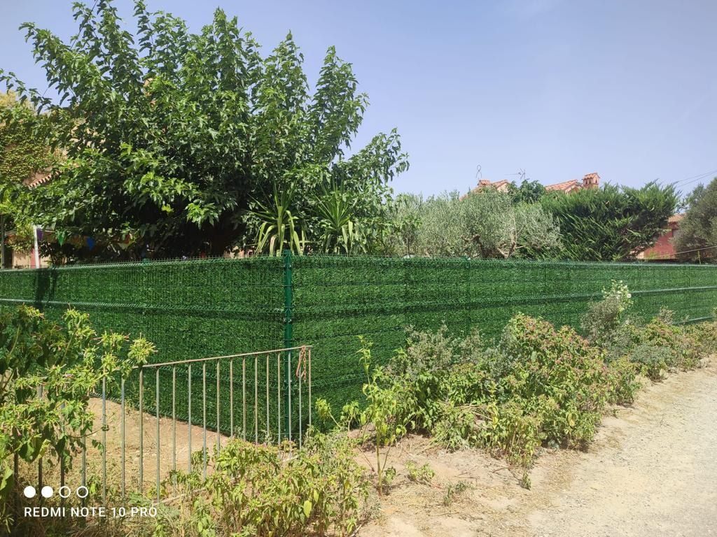 Una valla verde está rodeada de árboles y arbustos.