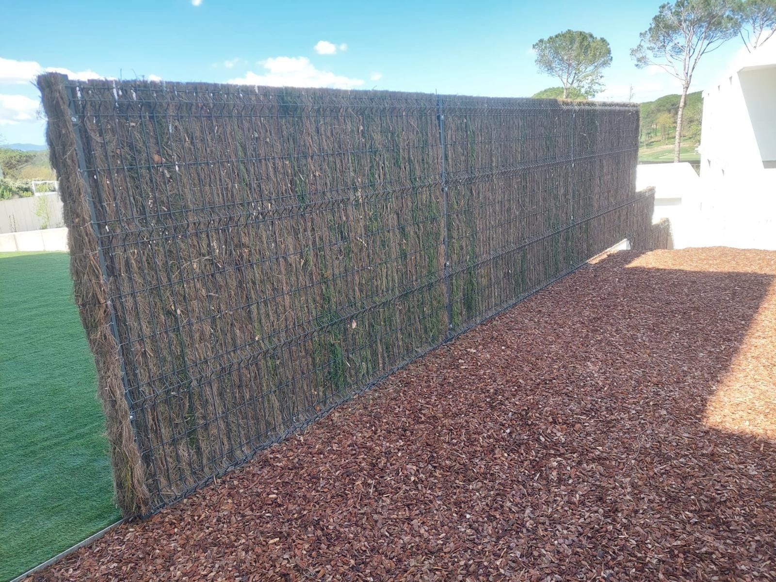 Una valla hecha de paja está situada al lado de una pila de mantillo.