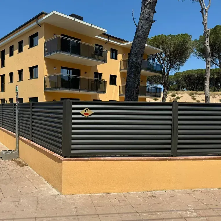 Un edificio amarillo con una valla negra delante.