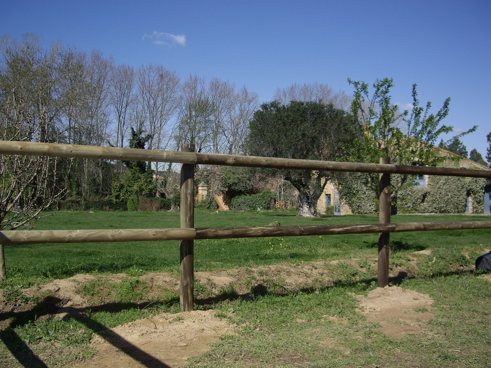 Una valla de madera rodea un campo de hierba con árboles al fondo.