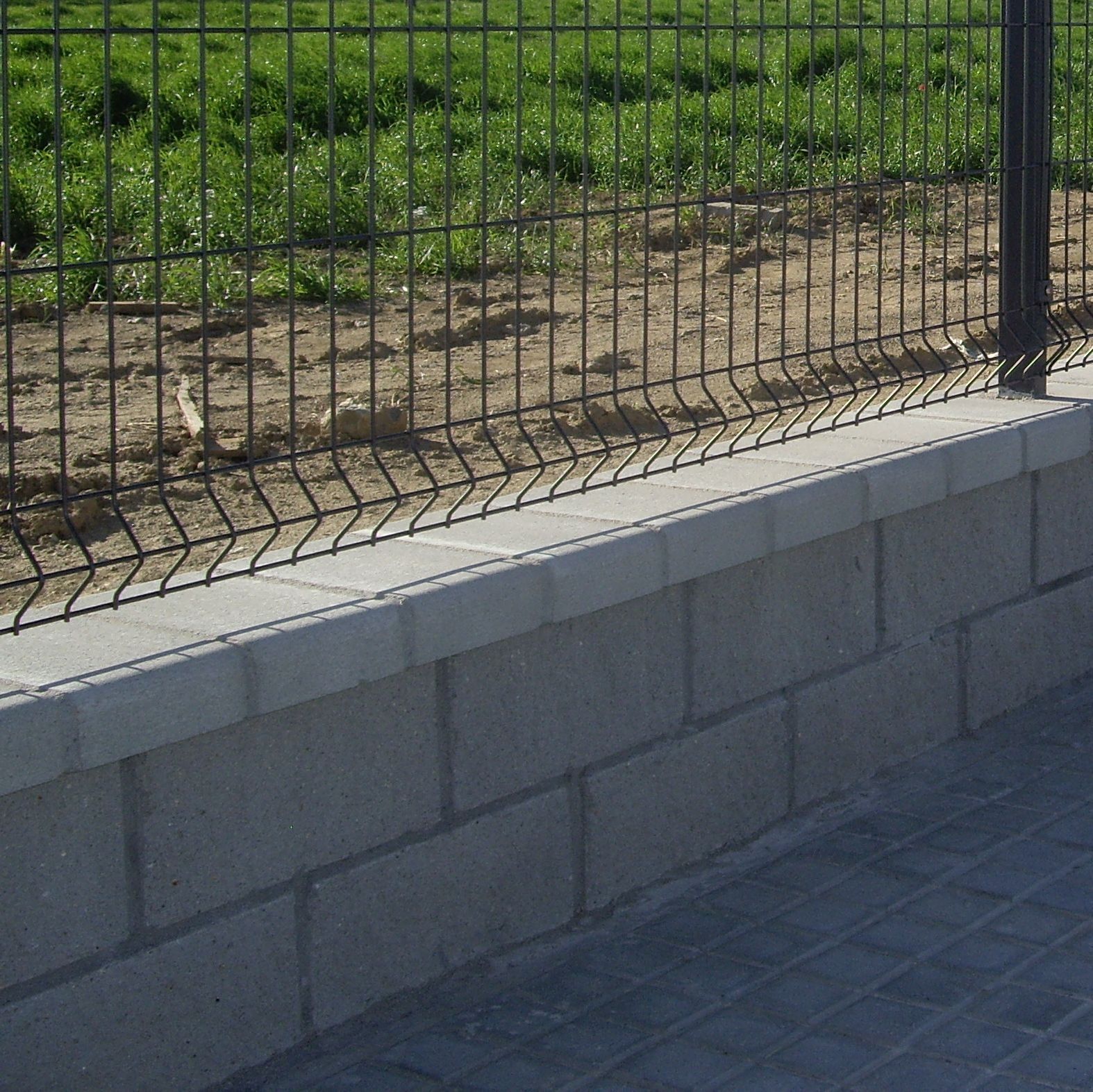 Una pared de ladrillos con una cerca de alambre detrás.
