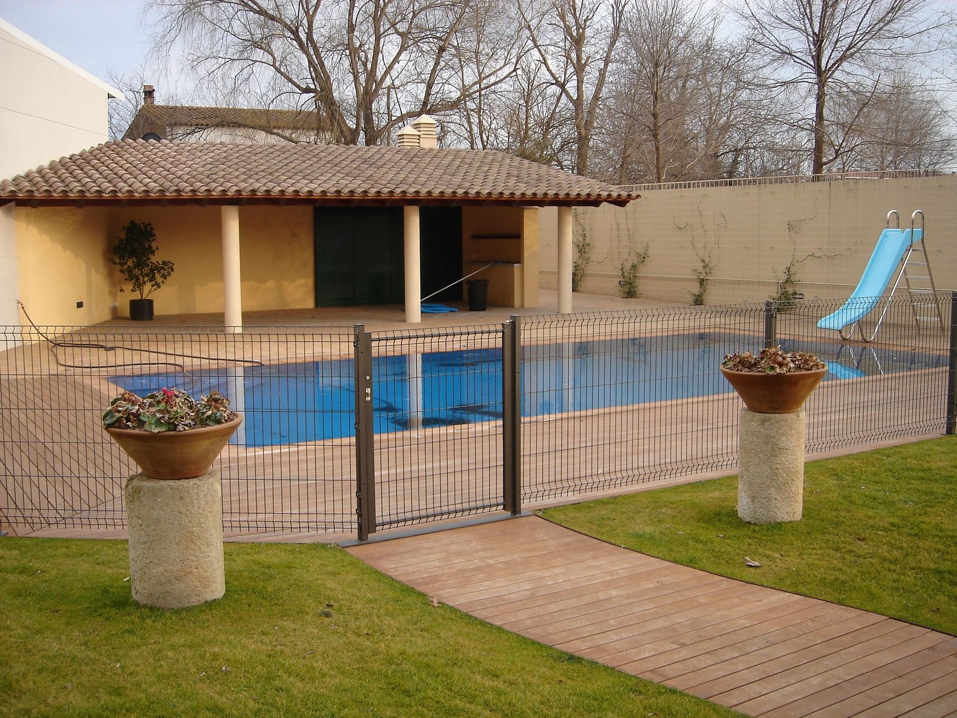 Una valla rodea una piscina con un pabellón al fondo.