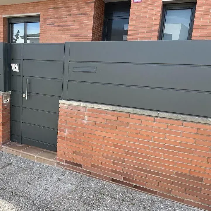 Un edificio de ladrillo con una valla negra y una puerta negra.