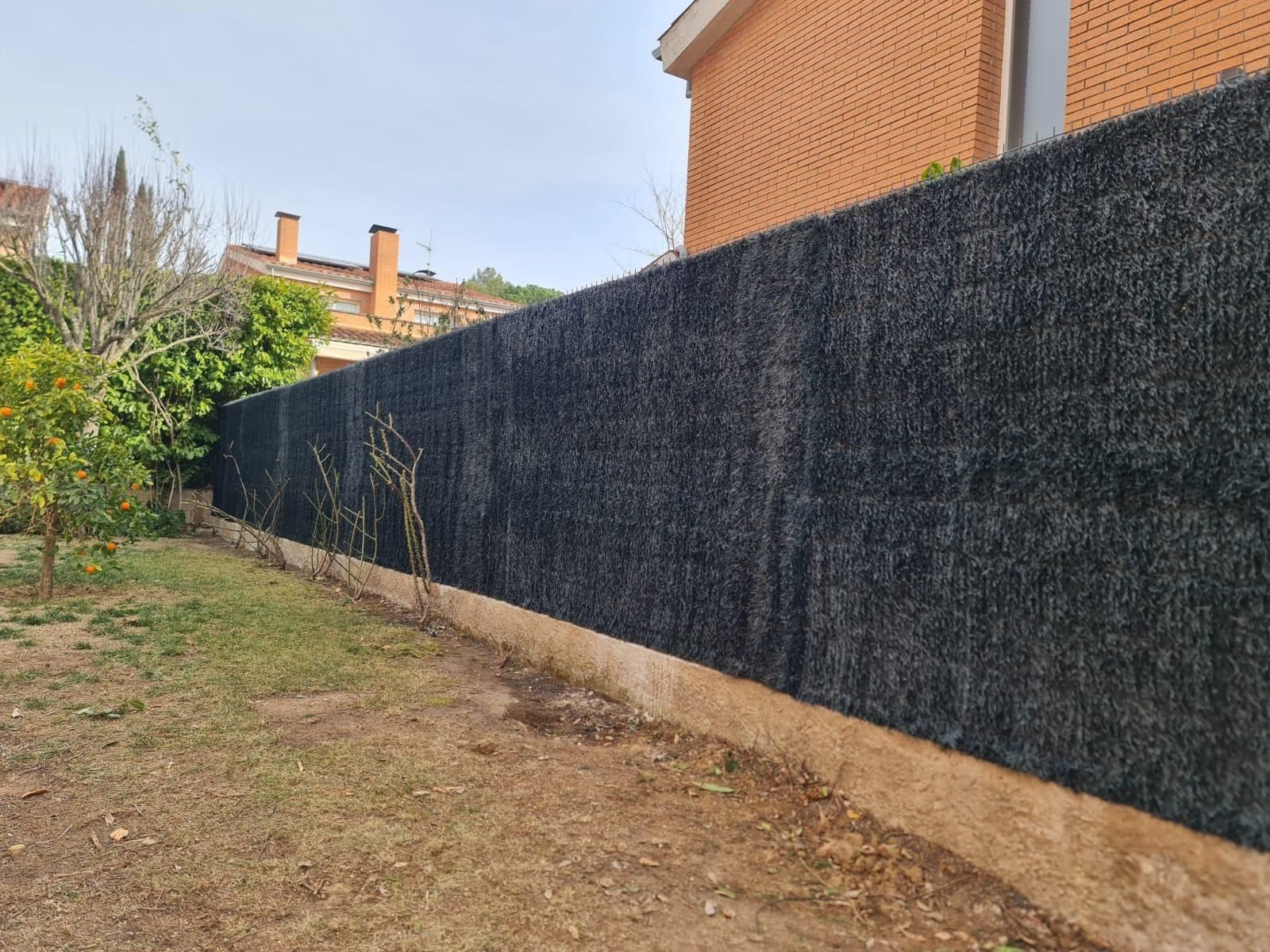 Una valla negra rodea una casa de ladrillo en un patio trasero.
