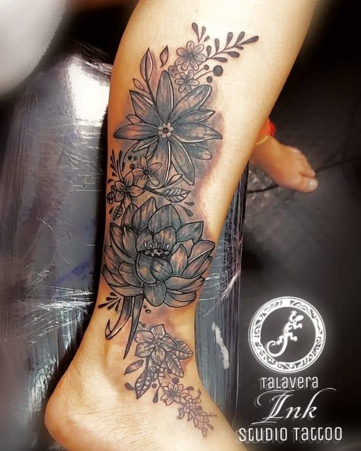 Parte inferior de la pierna con un gran tatuaje floral negro, con flores, hojas y una enredadera colgante