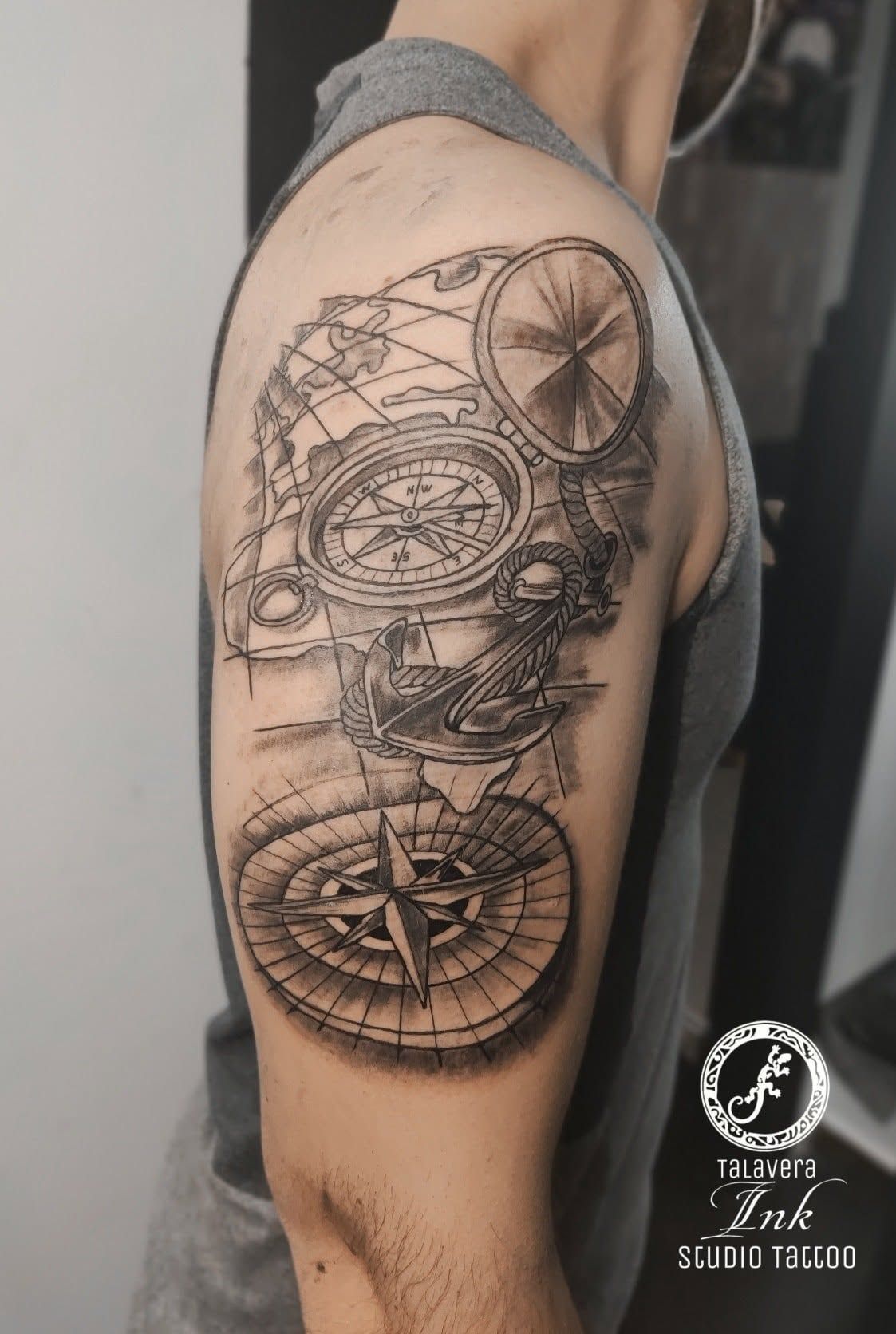 Vista lateral de un tatuaje en el hombro en negro y gris, con diseños geométricos y motivos similares a una brújula.