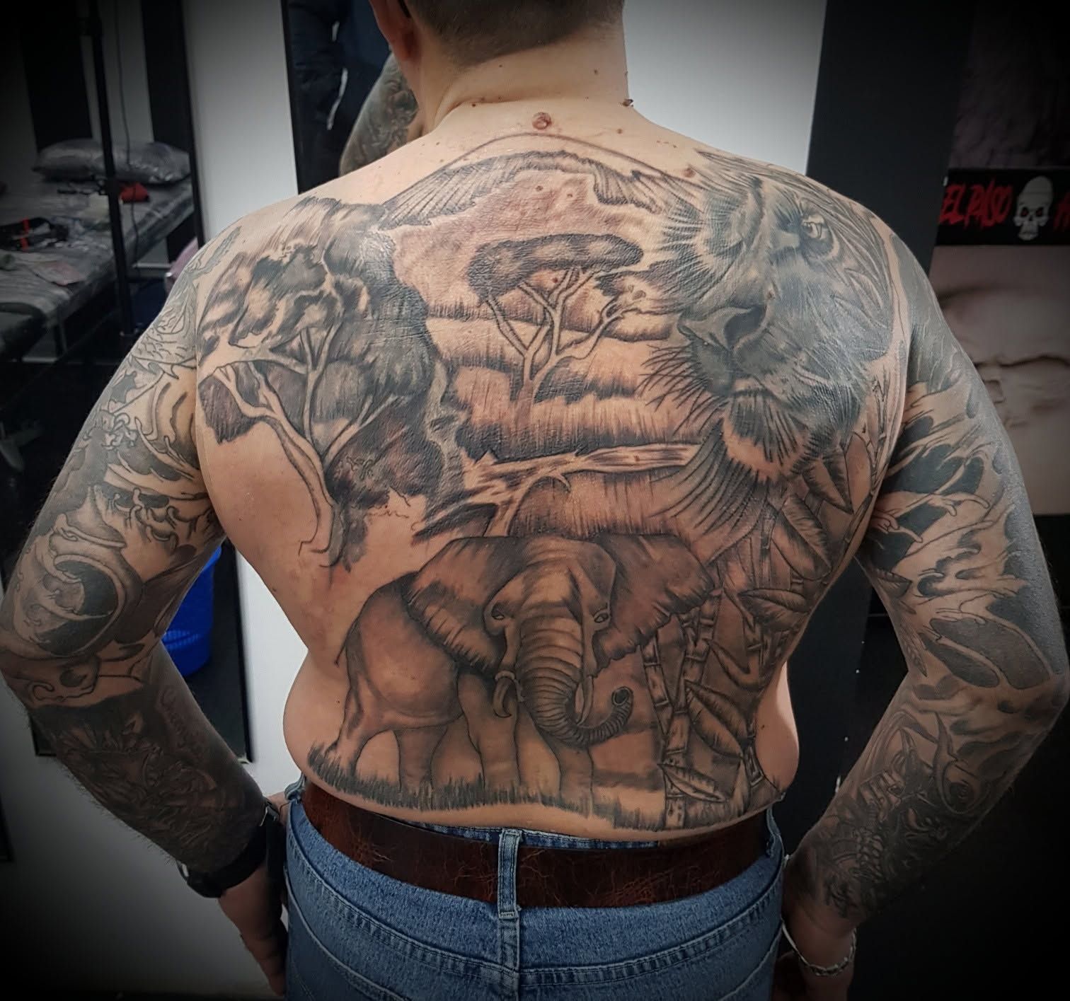 Hombre de espaldas mostrando un gran tatuaje negro y gris en la espalda, en un estudio de tatuajes