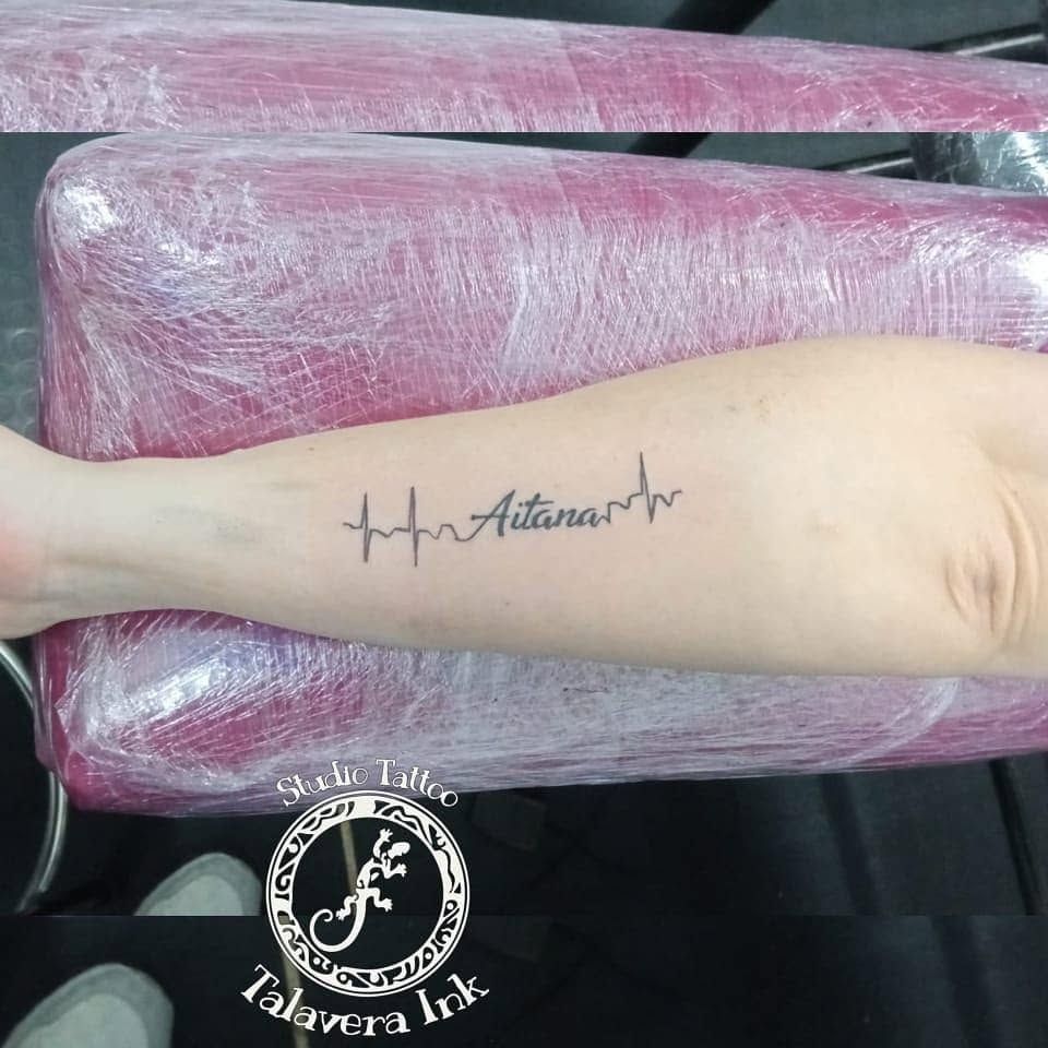 Antebrazo con una línea de latido y un tatuaje con el nombre «Aitana», apoyado sobre un cojín rosa