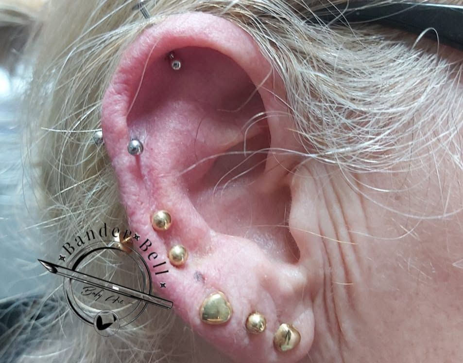 Primer plano de una oreja con varios pendientes dorados y plateados y cabello blanco cerca