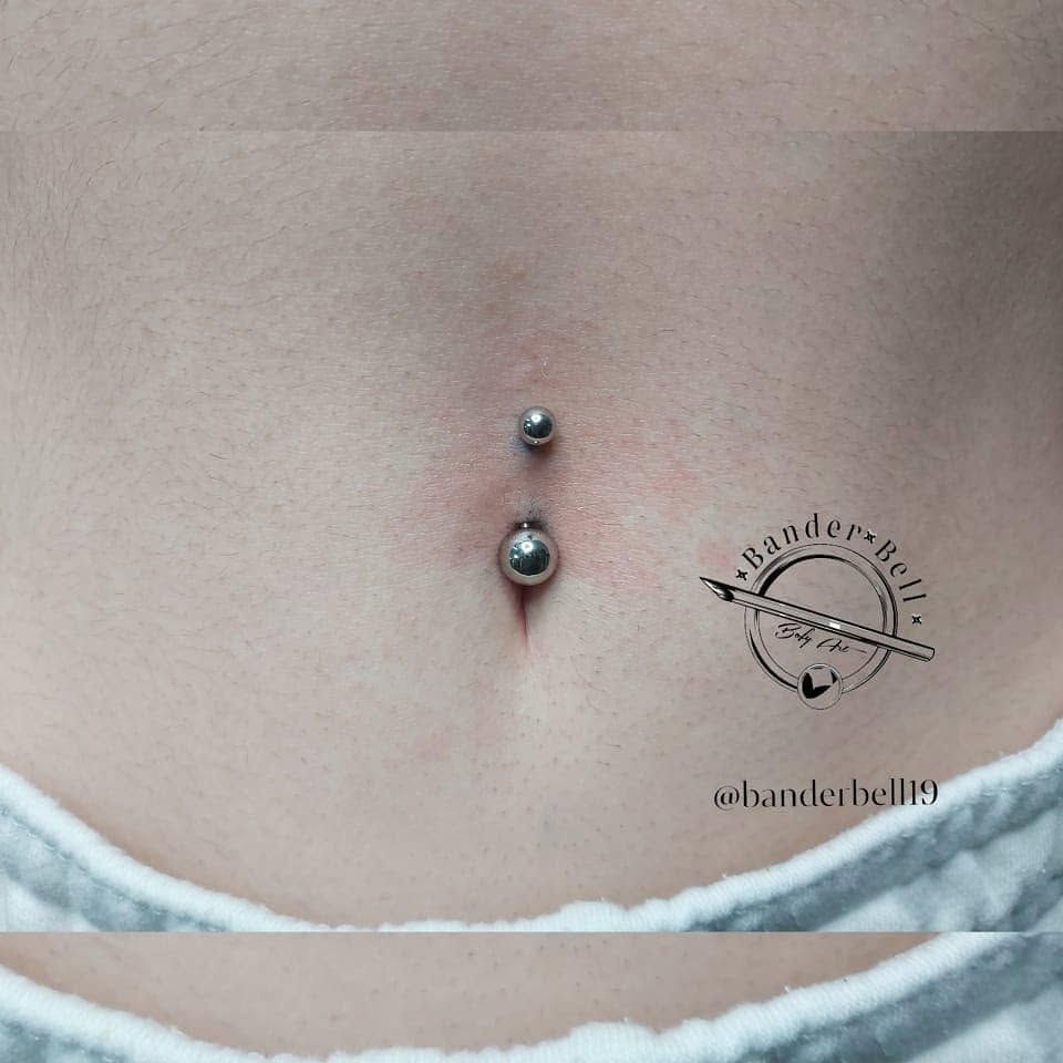 Primer plano de un piercing en el ombligo sobre la piel desnuda, con una joya plateada y una cinturilla blanca a la vista