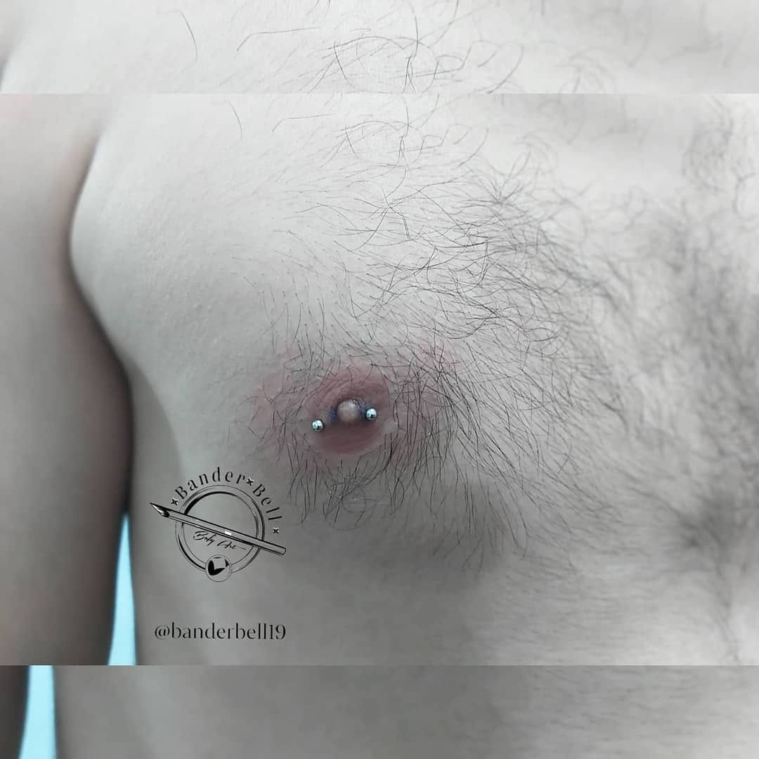 Primer plano de un pecho desnudo con un piercing en el pezón y vello visible en el pecho