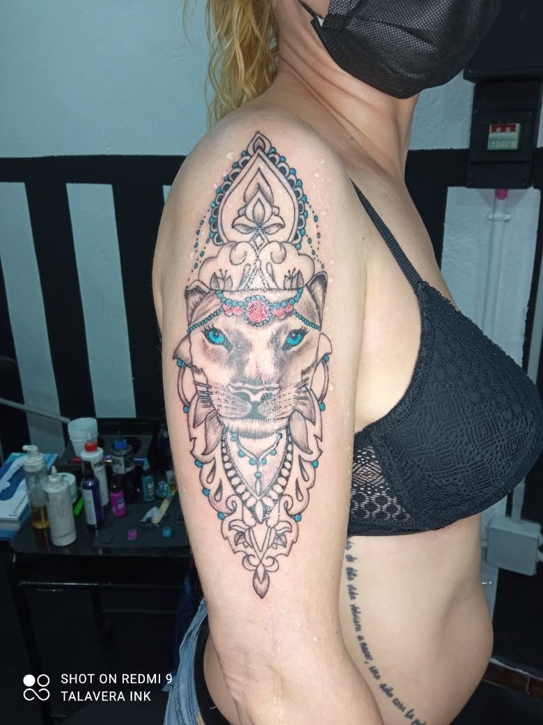 Vista lateral de una persona con un gran tatuaje colorido en el hombro y parte de otro en el abdomen, con una camiseta negra y mascarilla