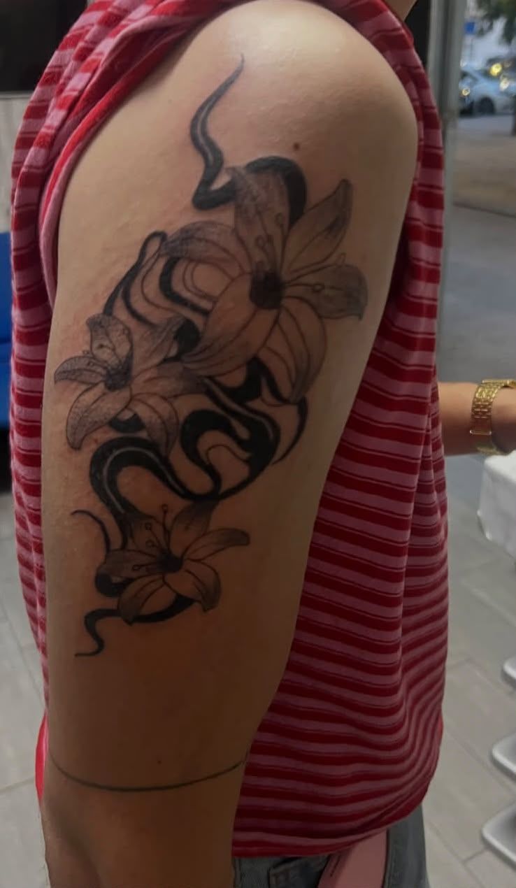 Brazo con un gran tatuaje floral negro en la parte superior, sobre una camisa a rayas rojas y en un entorno al aire libre.