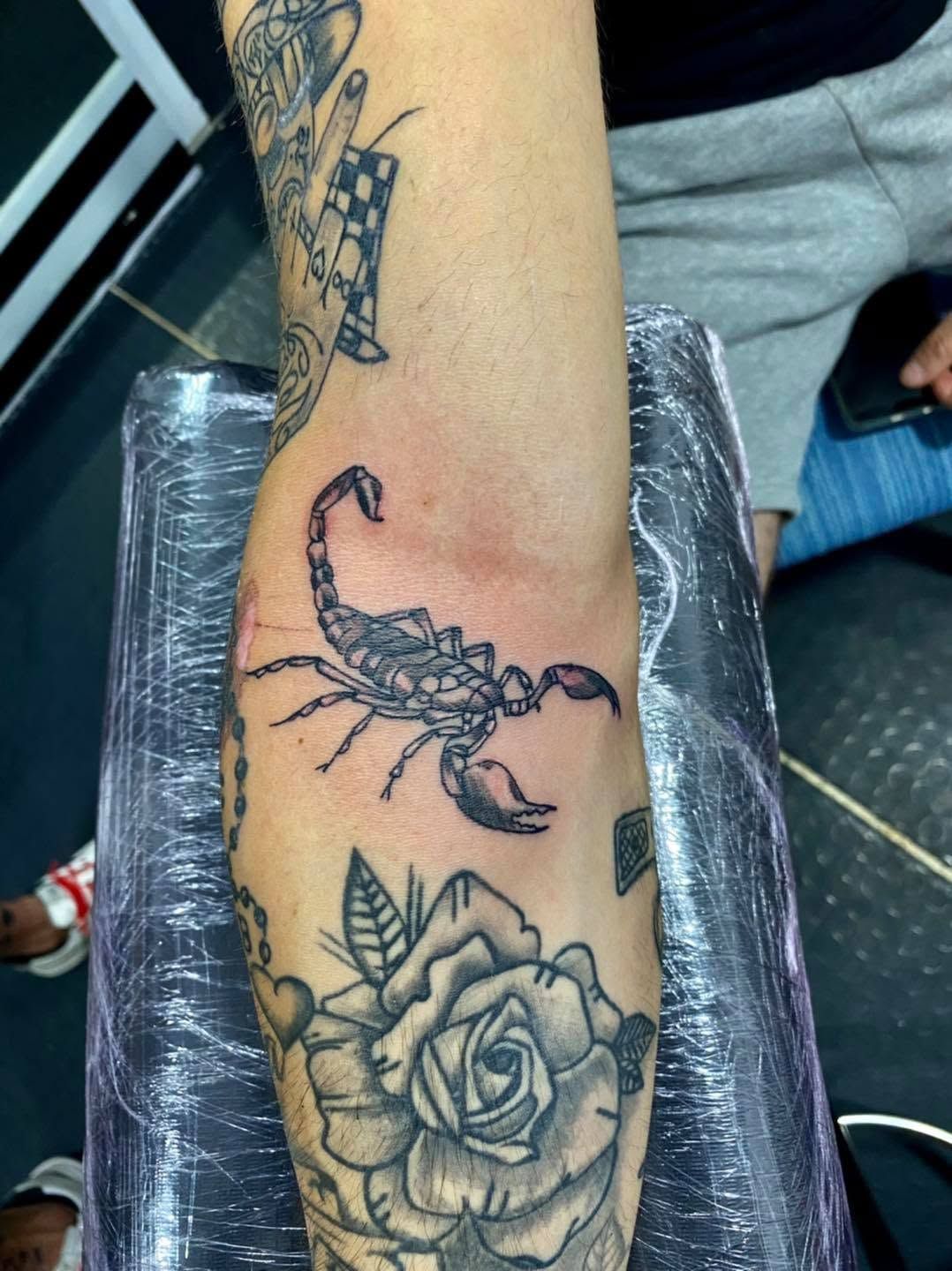 Tatuajes en el antebrazo de un escorpión negro y una rosa sobre piel clara, envueltos en plástico.