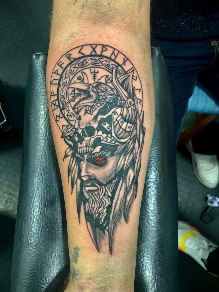 Primer plano de un antebrazo con un intrincado tatuaje de una calavera en negro y rojo con números romanos.