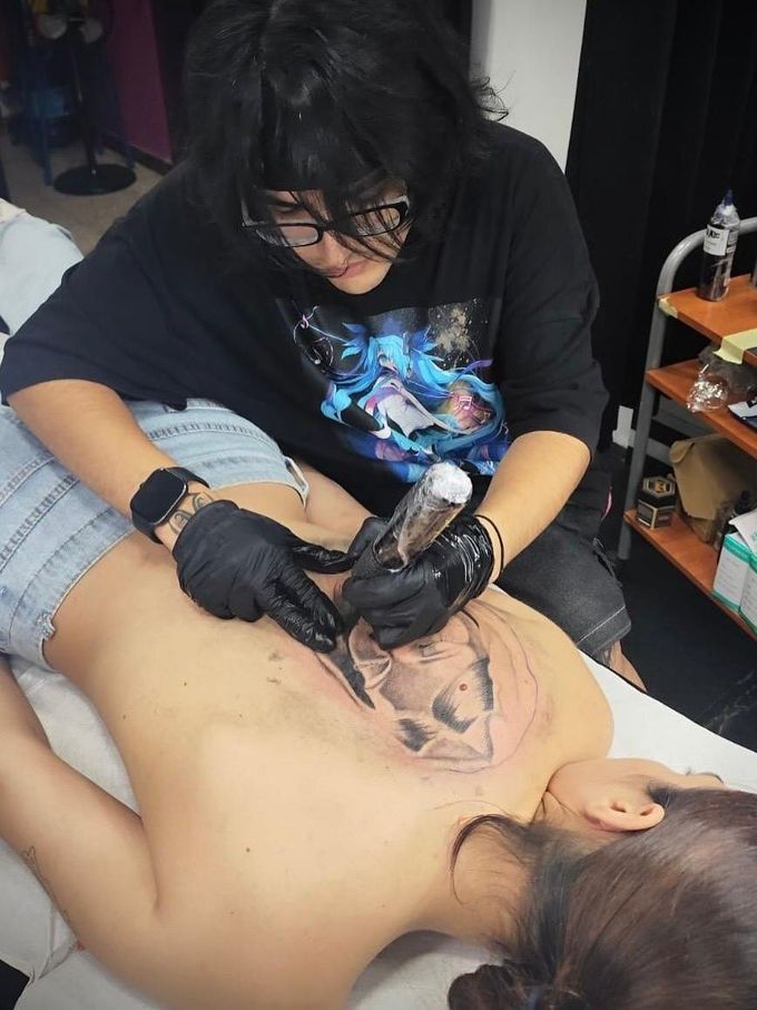 Un tatuador trabajando en un tatuaje en la espalda mientras el cliente está tumbado en una camilla